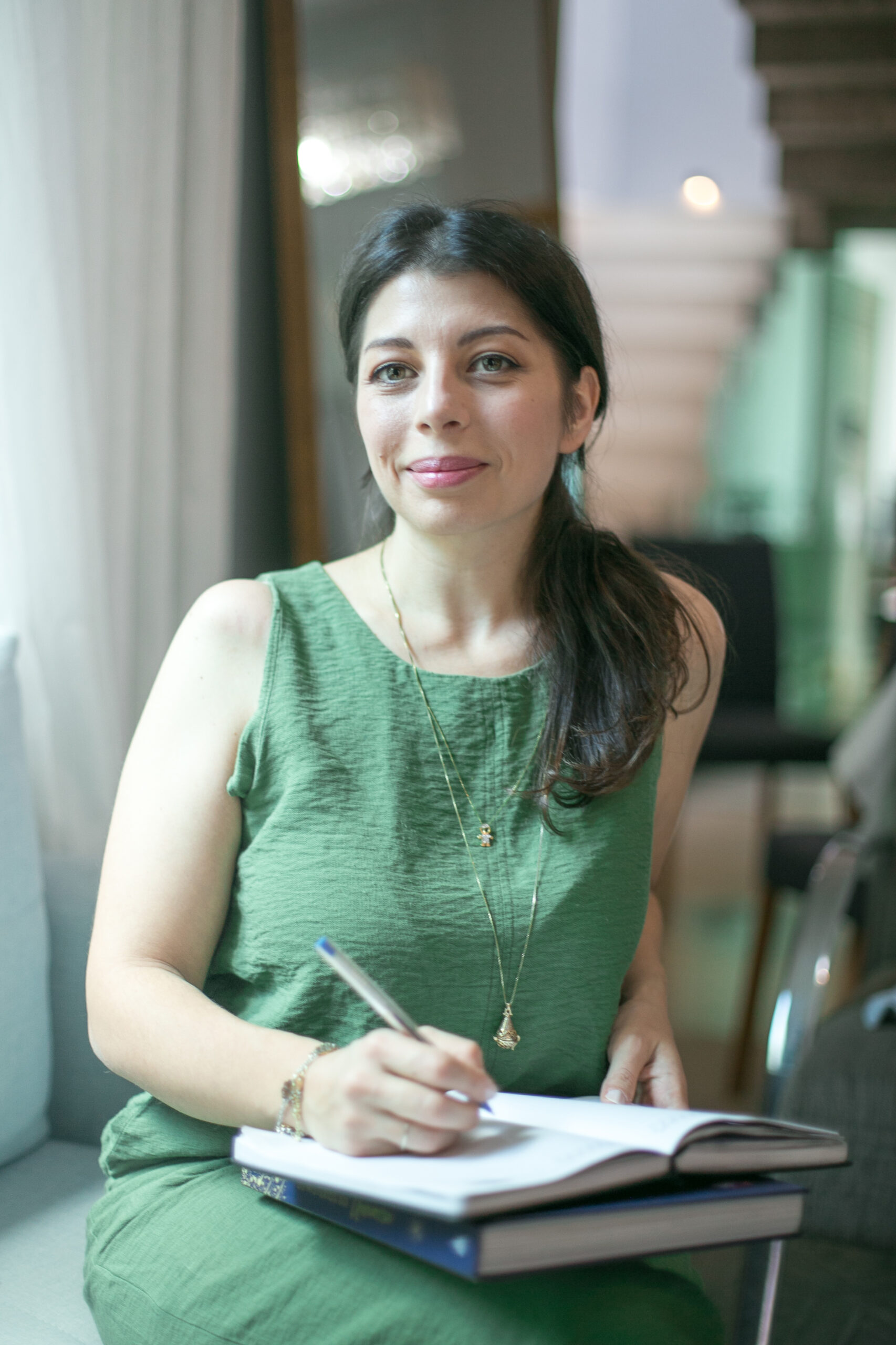 Irene Ferrazzuolo con un vestido verde está sentada en el interior, sonriendo suavemente con una expresión relajada.