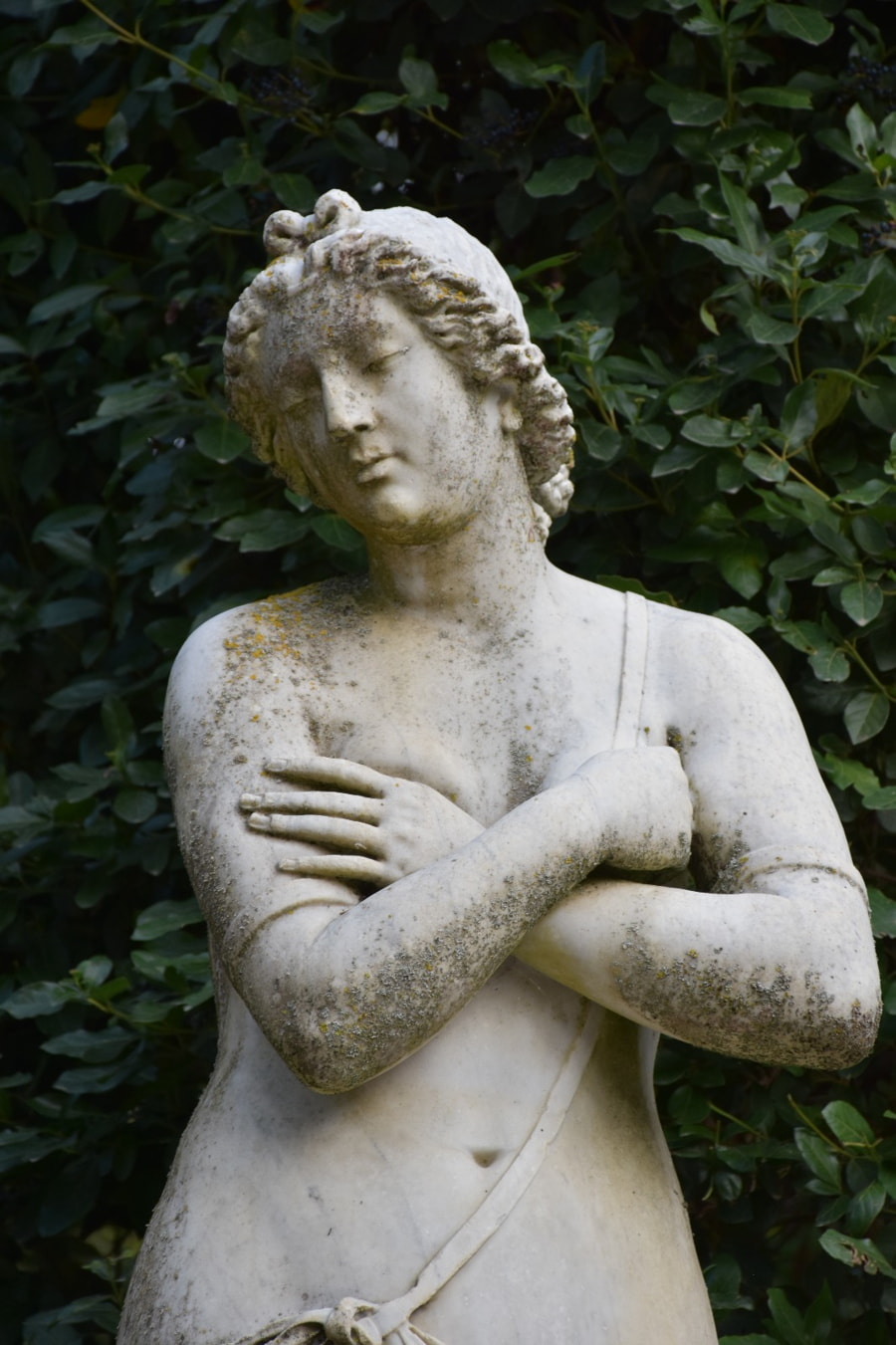 Estatua de mármol de una figura femenina serena con los brazos cruzados.