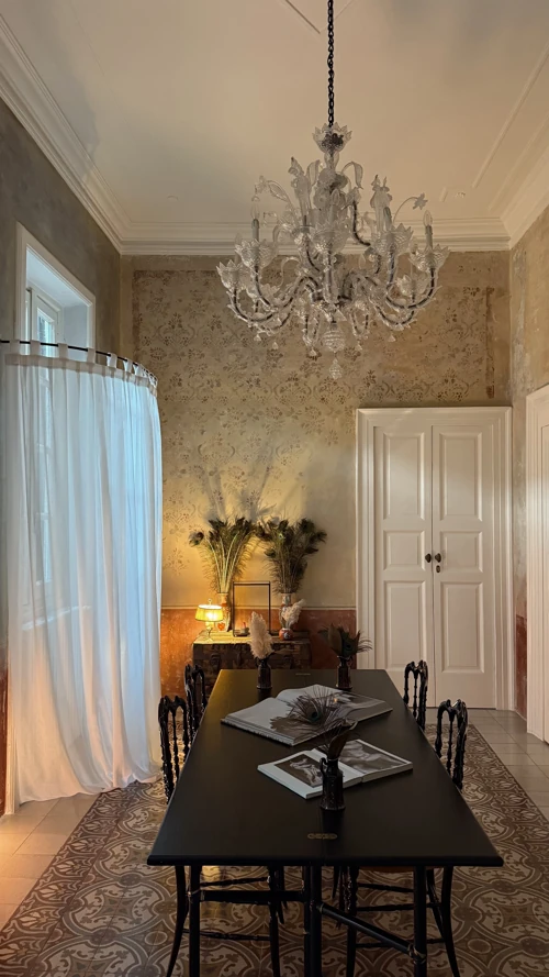 Elegante comedor con una mesa negra, sillas vintage y una lámpara de araña blanca. Elegante comedor con una mesa negra, sillas vintage y una lámpara de araña blanca.