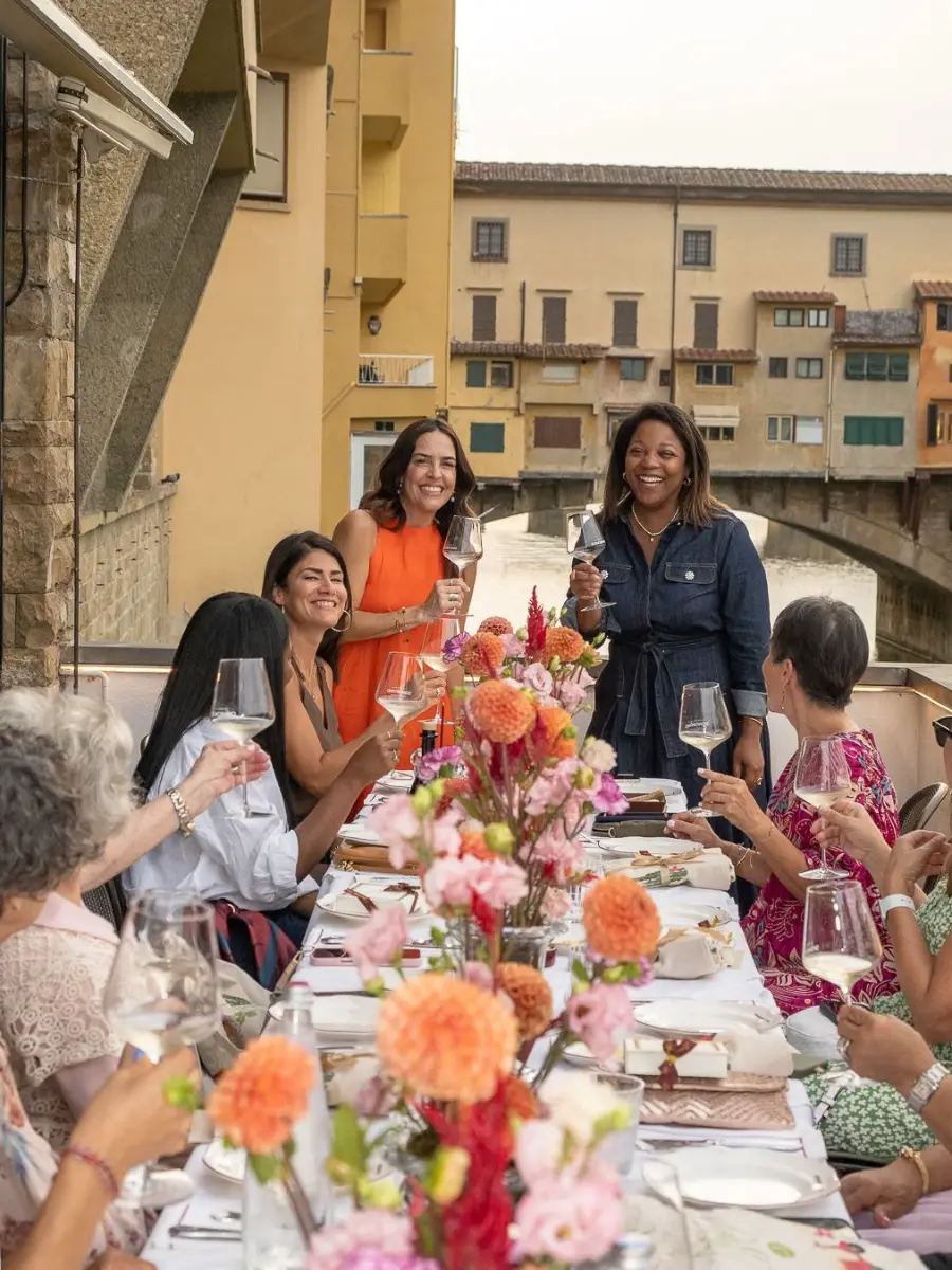 Viajeras brindando en una mesa con flores junto al Ponte Vecchio de Florencia