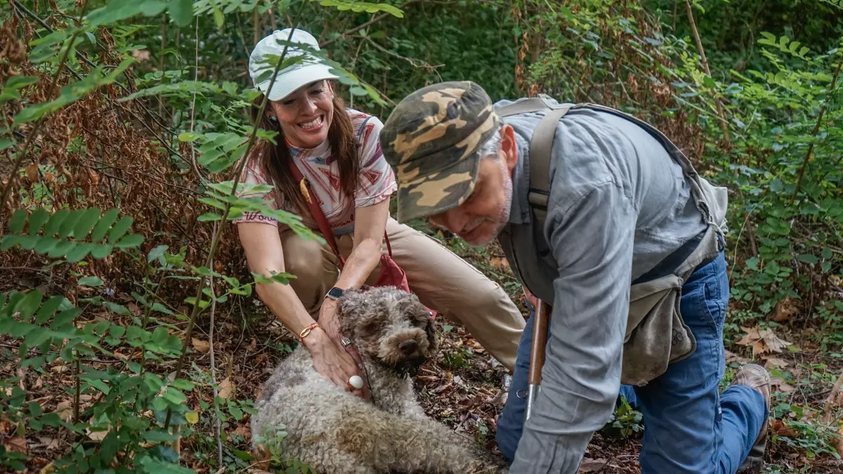 Viajera acariciando a un perro trufero junto a un buscador de trufas en el bosque toscano