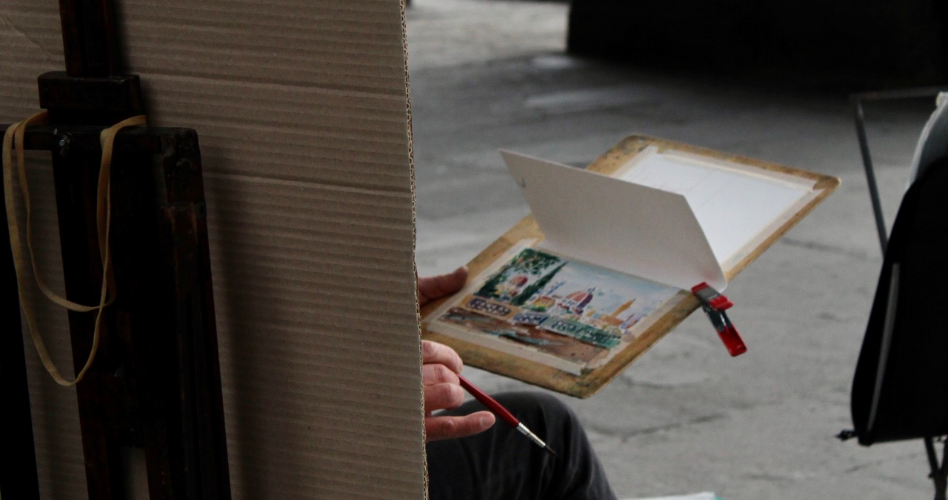 Viajes personalizados por Italia Artista pintando a mano una acuarela de una ciudad italiana con su cúpula, en plena calle